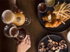 people are eating and drinking at a table with plates of food on it, along with glasses of beer