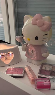 a hello kitty doll sitting on top of a counter next to makeup and eye shadow