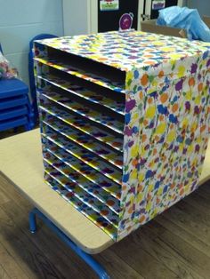 a stack of colorful boxes sitting on top of a wooden table next to a blue chair