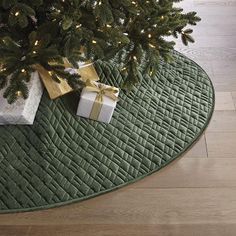 a christmas tree with presents under it on a green rug next to a white box