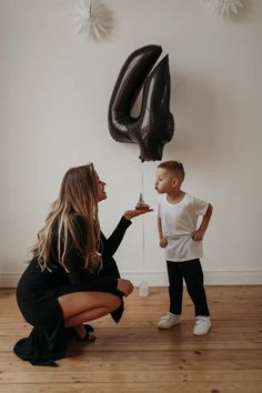 a woman kneeling down next to a little boy with a balloon in the shape of a number