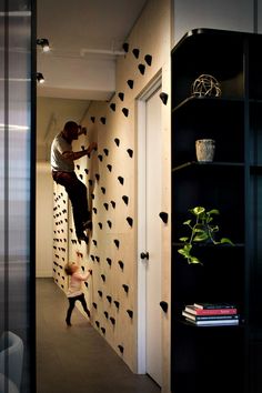 a man climbing up the side of a wall next to a book shelf and potted plant