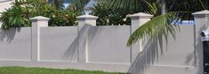 a white picket fence with palm trees in the back ground and a house behind it