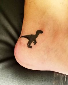 a small black dinosaur tattoo on the foot