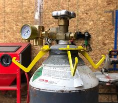 a propane gas bottle with yellow handles and nozzles on the top, sitting in front of a wooden wall