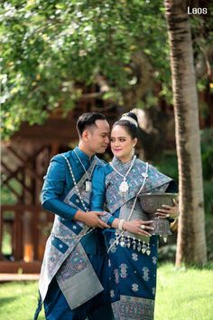 a man and woman standing next to each other in front of some trees with their arms around each other