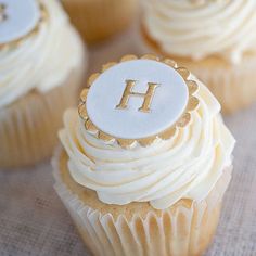 three cupcakes with white frosting and gold trim, each decorated with the letter h