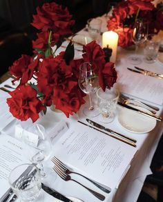 the table is set with silverware and red flowers