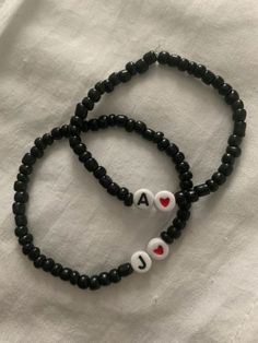 two black beaded bracelets with white and red letters on them, one has a heart in the middle