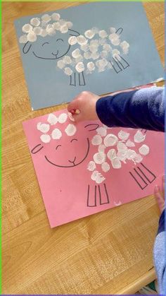 a child's hand is drawing on paper with flowers and sheeps in the background