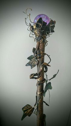 a tall metal pole with vines on it and a purple ball in the middle, sitting against a white wall