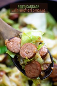 a wooden spoon filled with sausage and lettuce on top of a bed of salad