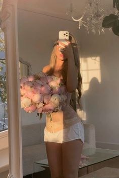 a woman taking a selfie in front of a mirror holding a bouquet of flowers