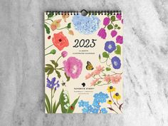 a calendar with flowers on it sitting on top of a marble table next to a plant