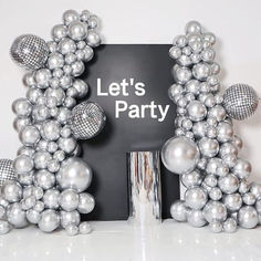 a party sign surrounded by silver balloons and disco ball decorations on a white table with the words let's party written below it