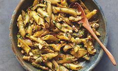 a bowl filled with pasta and vegetables on top of a table next to a wooden spoon