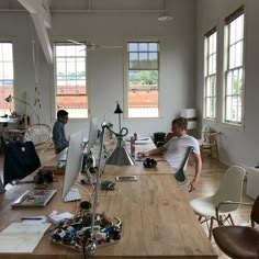 two men sitting at desks in an office with lots of clutter on the floor