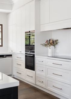 a large kitchen with white cabinets and black stove top oven in the center, surrounded by wood flooring