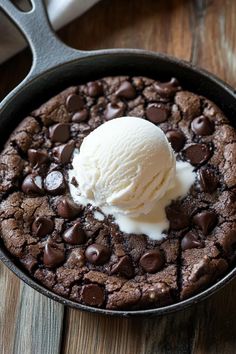 a chocolate skillet cake with ice cream in it on a wooden table next to utensils