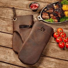 a grilling mitt next to a plate of food on a wooden table with tomatoes and corn