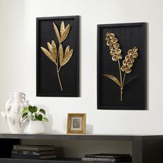 two black and gold framed art pieces on a white wall next to a vase with flowers