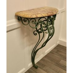 an iron and marble console table against a white wall with wood flooring in the corner