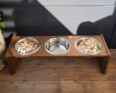 three metal bowls with food in them on a wooden stand