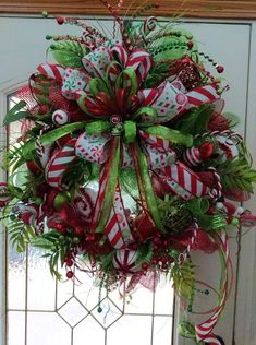 a christmas wreath with candy canes and bows hanging from the front door, decorated with greenery