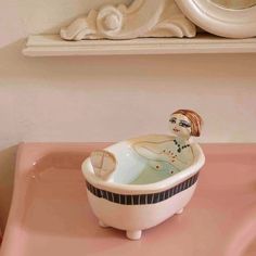 a ceramic bowl sitting on top of a pink counter next to a white framed mirror