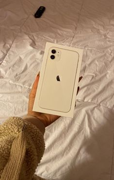 a person holding an iphone in their hand on top of a white sheet covered bed