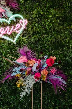 a neon sign that says love on top of a table with flowers and greenery