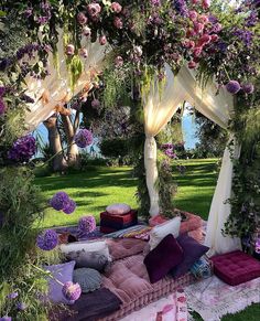 an outdoor area with flowers and pillows on the ground, in front of a gazebo