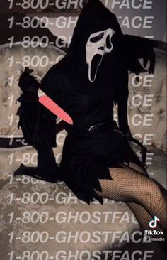 a woman in a black costume sitting on a couch with a knife and mask over her face