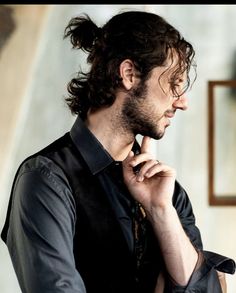 a man with curly hair is wearing a black shirt and looking off to the side