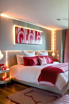 a bed with red and white pillows on top of it next to a wall mounted painting