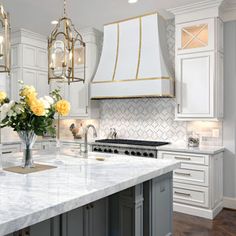 a large kitchen with marble counter tops and white cabinets, along with yellow flowers in a vase