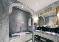 a bathroom with marble walls and flooring has a large mirror over the bathtub