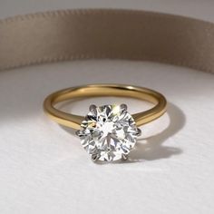 a close up of a diamond ring on a white surface with a beige ribbon around it