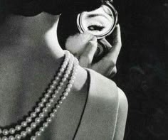 a woman holding a cell phone up to her ear while wearing pearls and a necklace