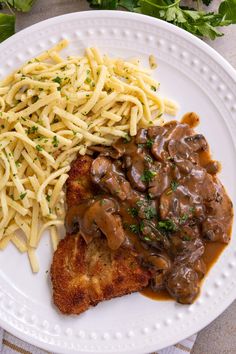 a white plate topped with meat covered in gravy next to pasta and french fries