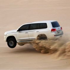 a white truck is driving through the sand in the middle of the desert with dust coming off it's tires