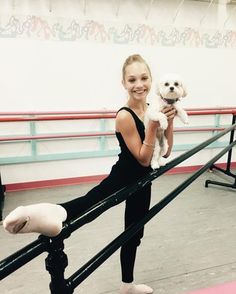 a woman holding a small white dog on top of a rail in a dance studio