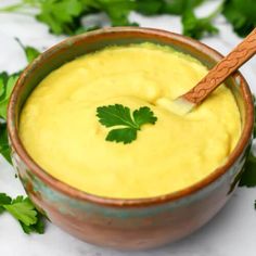 a wooden spoon in a brown bowl filled with yellow sauce and garnished with parsley