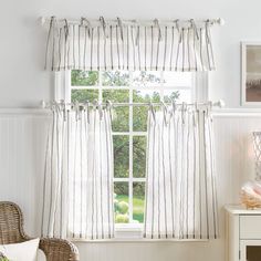 a chair and window in a room with white paint on the walls, striped curtains, and wicker furniture