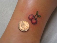 a small tattoo on the ankle of a woman with two cherries and a penny