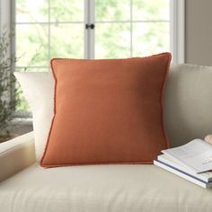 an orange pillow sitting on top of a white couch next to a book and plant