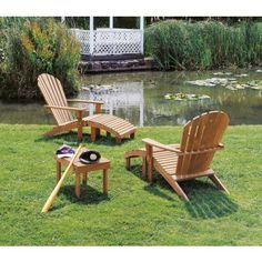 three wooden lawn chairs sitting on top of a lush green field next to a pond