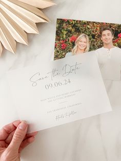 a person holding up a wedding save the date card