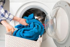 a person is doing laundry in front of a washing machine with blue towels and a basket