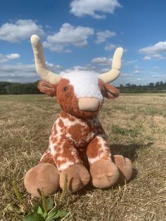 a brown and white stuffed cow sitting in the grass with its horns spread wide open